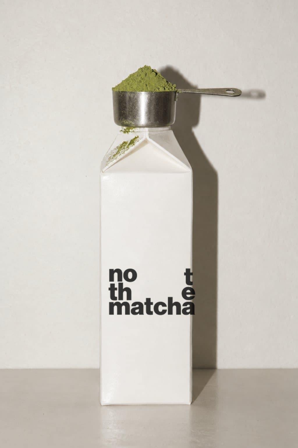 A measuring cup heaped with matcha on top of a milk carton