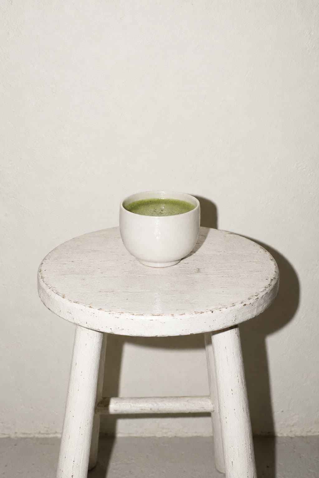 A small white cup of whisked matcha on a white stool
